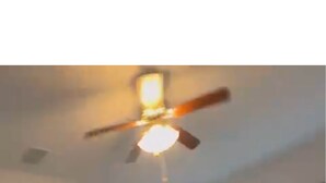 Un dormitorio con cama, mesita de noche, ventilador de techo y ventanas grandes.