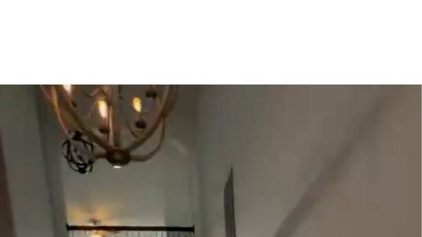 Un amplio pasillo con suelo de madera, un candelabro y una escalera que sube a otro nivel.