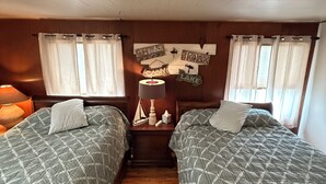 A cabin-style room with two beds, wooden walls, and a ceiling with exposed beams.