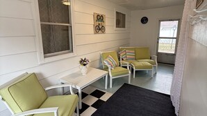 A room with a checkered floor, two green chairs, a white table, and a small window.