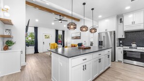 Uma cozinha moderna com armários brancos, uma ilha central, eletrodomésticos de aço inoxidável e iluminação pendente.
