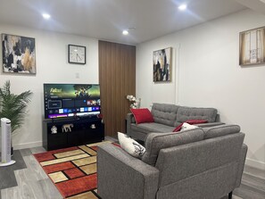 Ein modernes Wohnzimmer mit Flachbildfernseher, grauem Sofa, roten Kissen und einem gemusterten Teppich.