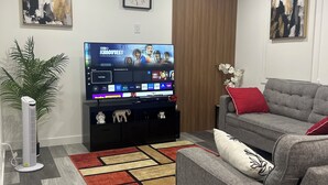 Een moderne woonkamer met een flatscreen televisie, een grijze bank, rode kussens, een decoratief vloerkleed en een wandklok.