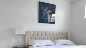 Een moderne slaapkamer met een gestoffeerd hoofdeinde, een nachtkastje met een lamp en een groot bed met witte beddengoed.