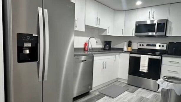 Een moderne keuken met roestvrijstalen apparatuur, witte kastjes en een grijze houten vloer.