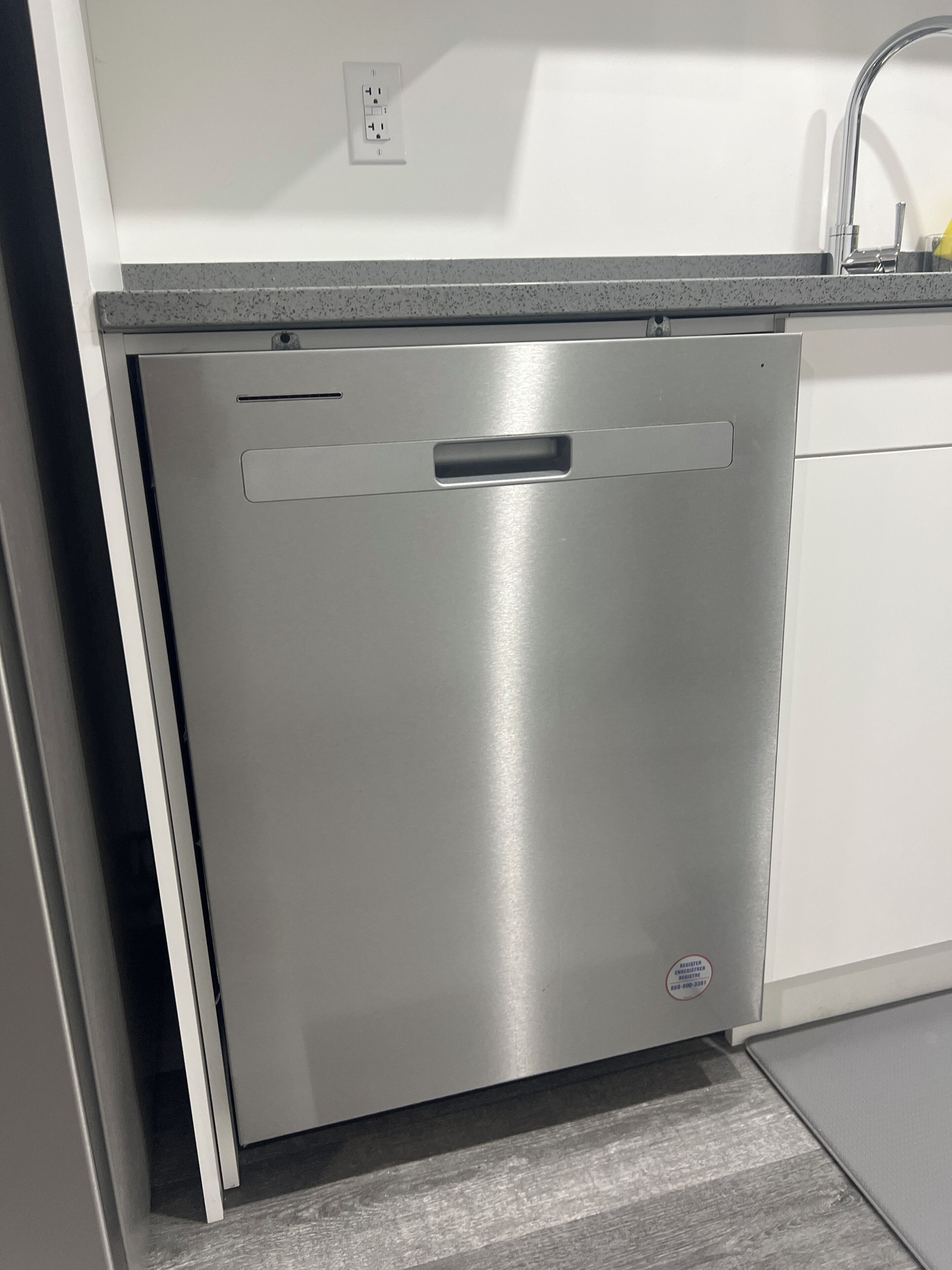 A stainless steel dishwasher in a kitchen with a grey countertop and a white wall.