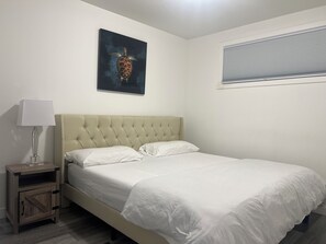 Ein Schlafzimmer mit einer geblatteten Kopfteile, einem Einzelbett mit weißer Bettwäsche, einem Nachttisch mit Lampe und einem gerahmten Kunstwerk an der Wand.