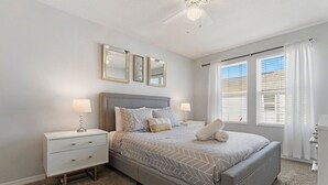 Een slaapkamer met een bed, twee nachtkastjes, een ventilator in het plafond en een raam met jaloezieën.