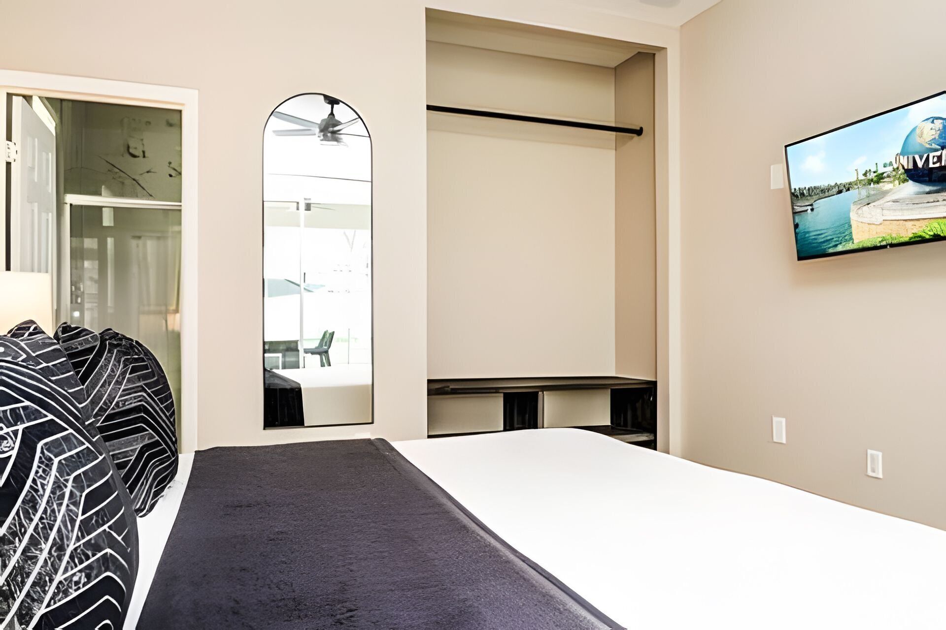 A hotel room with a bed, a TV mounted on the wall, a ceiling fan, and a view of a building outside.