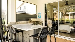 A modern outdoor kitchen area with a dining table and chairs, a built-in grill, and a sliding glass door leading to a patio.