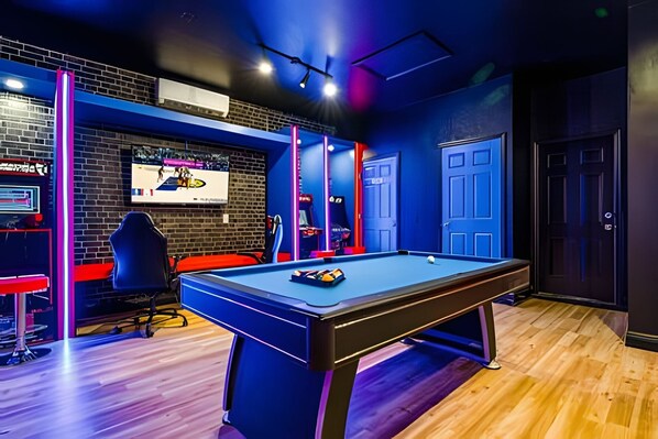 Une table de billard dans une pièce avec un mur en briques, un téléviseur fixé au mur et des néons.