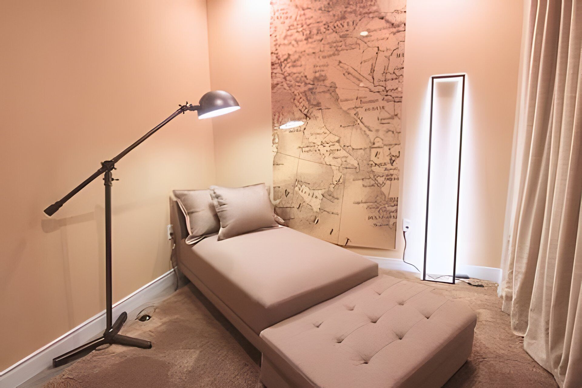 A bedroom with a bed, a reading lamp, a map on the wall, and a door.