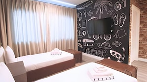 Ein Hotelzimmer mit zwei Betten, einem Flachbildfernseher und einer Wand mit Reise-Illustrationen.