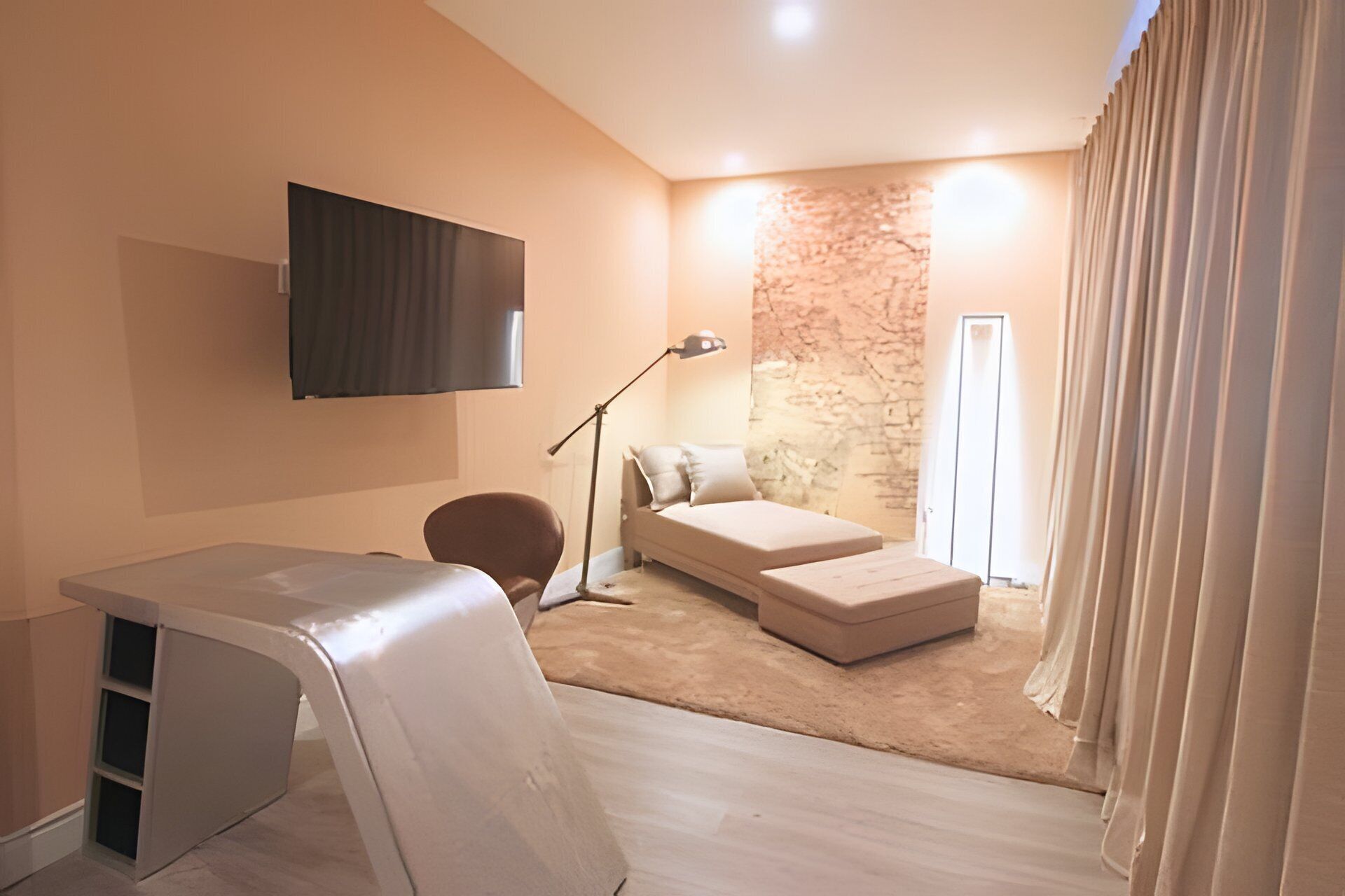 A modern bedroom with a bed, a desk, a chair, and a TV mounted on the wall.