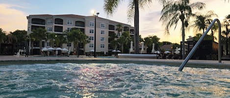 Um hotel com piscina, palmeiras e um pôr do sol.