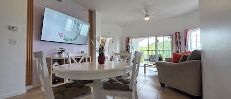 A modern living room with a dining area, a ceiling fan, a flat-screen TV, and a view to the outside.