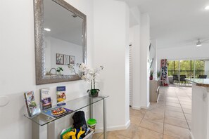 Et moderne interiør med et glasbord der fremviser magasiner og en grøn plante, et stort spejl og udsigt til en udendørs patio.