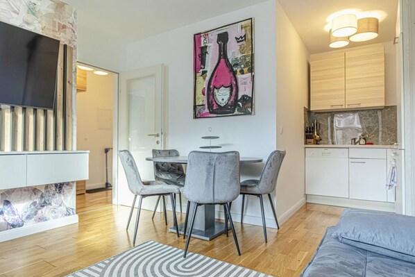 A modern living room with a TV, grey chairs, a dining table, and a kitchen area with cabinets and a countertop.