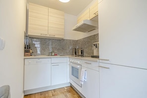 A compact kitchen with white cabinetry, a built-in oven, and a coffee maker.