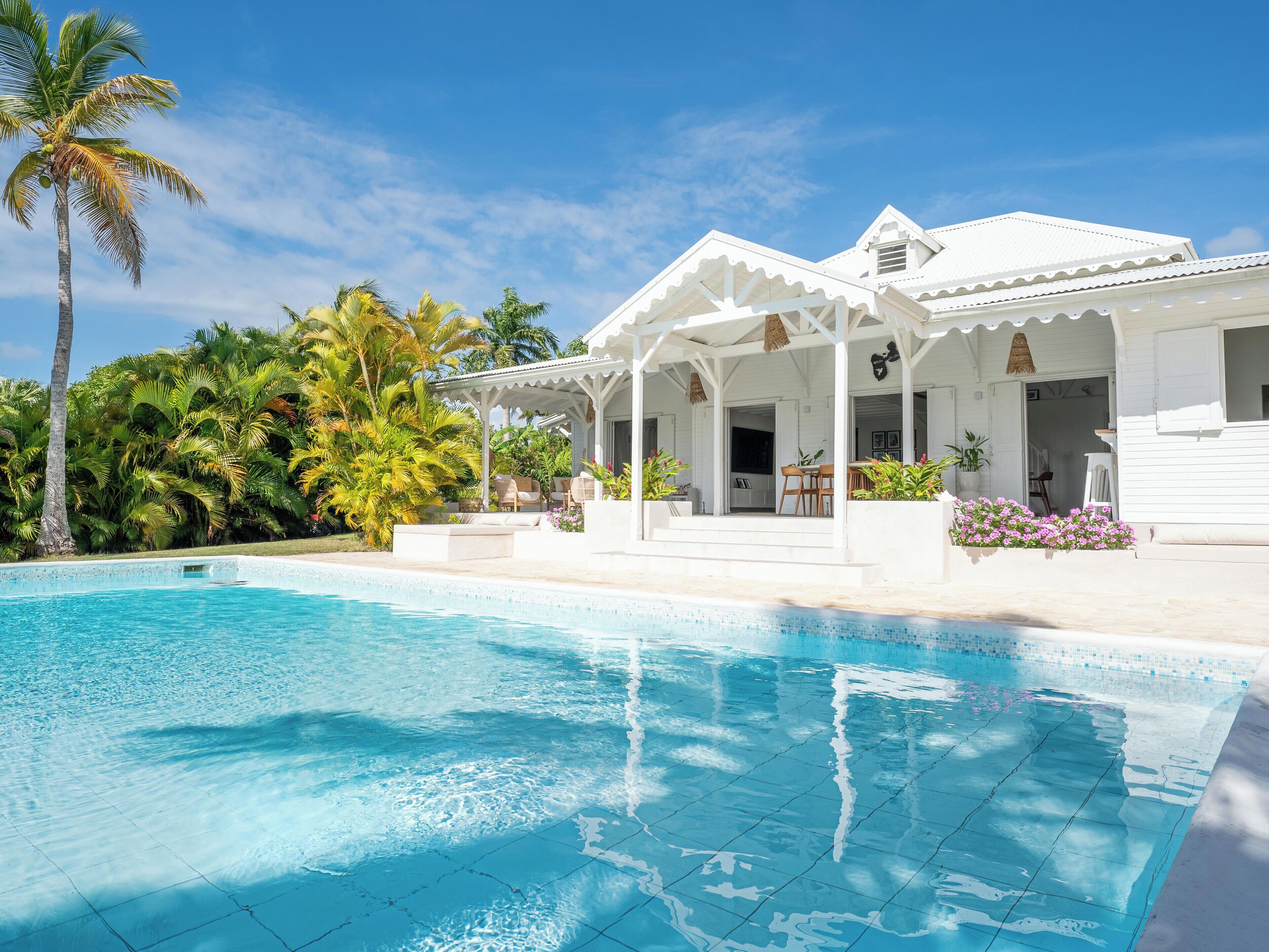 Eine weiße Villa mit Pool, umgeben von Palmen und tropischer Vegetation.