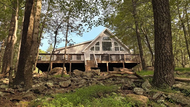 A cabin with a wooden deck, large windows, and a stone foundation. - Chickadee Retreat - Creekside Pocono Forest, fireplace, games, pool, lakes (Albrightsville)
