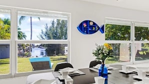 Ein Essbereich mit Blick auf einen Pool und Bäume, ein blaues, fischförmiges Regal und eine Vase mit Blumen.