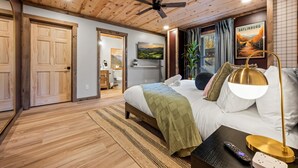 Ein Schlafzimmer mit Holzbalkendecke, einem Bett mit grüner Decke, einem Nachttisch mit Lampe, einer Fernbedienung und einem Poster von Gatlinburg.