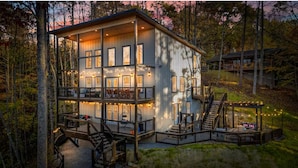 Eine zweistöckige Holzhütte mit einer Terrasse, umgeben von Bäumen, mit zahlreichen Fenstern und einer Treppe.
