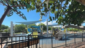 A playground with various play structures, including slides and climbing areas, surrounded by a fence and trees. - #10 Unit in Mid-century Art-Déco Building KingBed EnSuiteBath Steps>Beach PetsOK (Miami Beach)