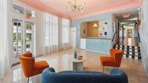A lobby with a reception desk, two orange armchairs, a blue sofa, and a chandelier. - #10 Unit in Mid-century Art-Déco Building KingBed EnSuiteBath Steps>Beach PetsOK (Miami Beach)