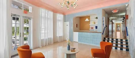 A lobby with a reception desk, two orange armchairs, a blue sofa, and a chandelier.
