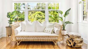 A rattan sofa with white cushions and a woven bench, positioned in front of a large window with a view of lush greenery. - FlipFlopsOn III • 1/2 Mile to Siesta Key • FL’s Gulf Coast • Sarasota (Sarasota)