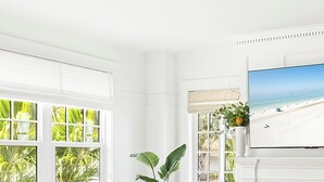 A bright, white room with a large window, a white sofa, a television, and a fireplace. - FlipFlopsOn III • 1/2 Mile to Siesta Key • FL’s Gulf Coast • Sarasota (Sarasota)