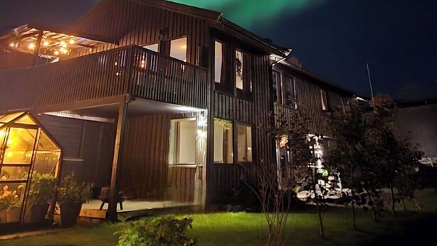 Una casa de madera de dos pisos con un balcón, bajo un cielo nocturno con la aurora boreal.