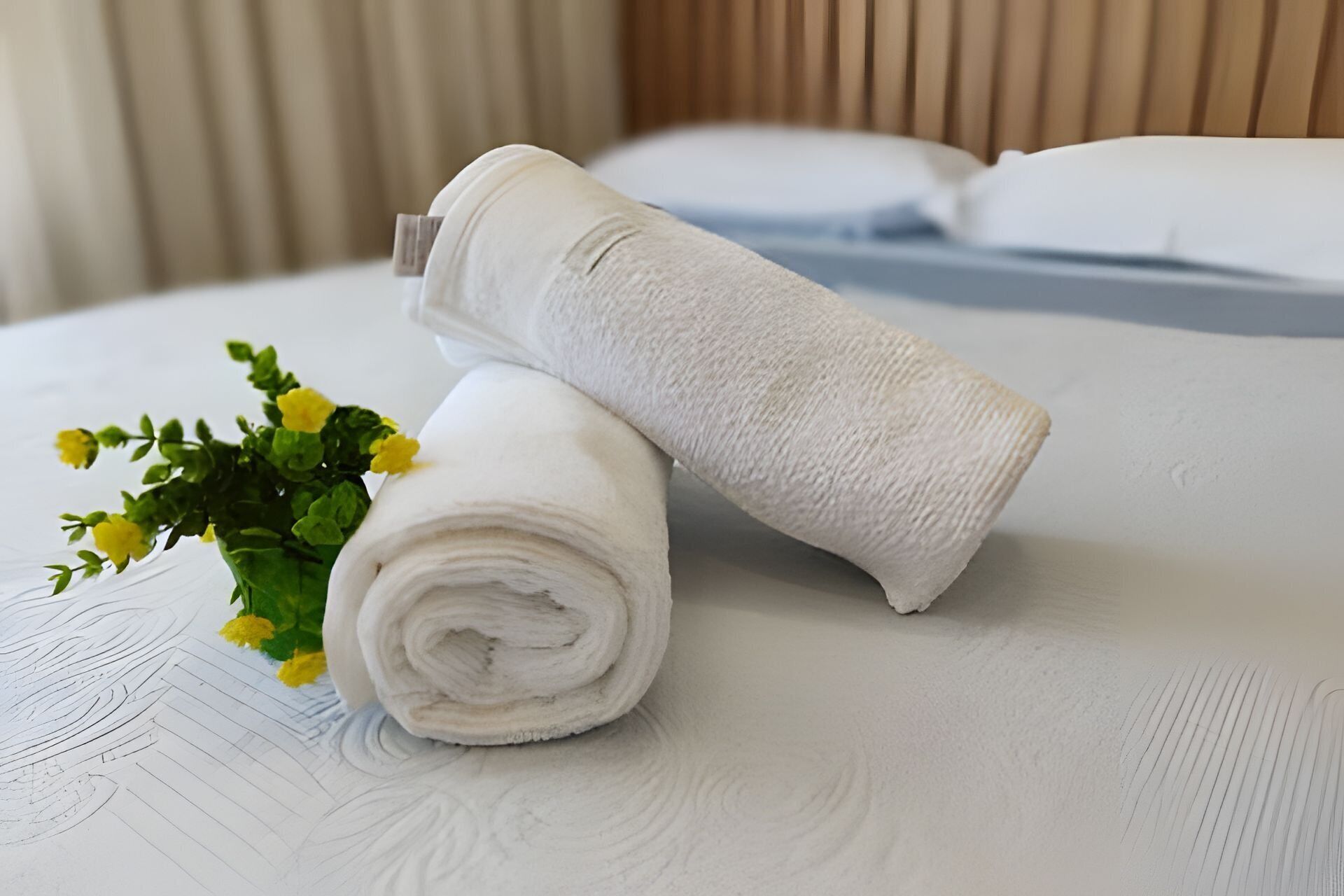 A neatly made bed with white linens and a small bouquet of yellow flowers.