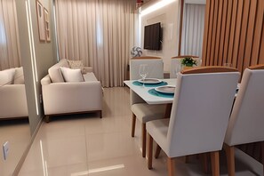 Una sala de estar moderna con un sofá, una mesa de comedor con sillas y un televisor de pantalla plana montado en la pared.
