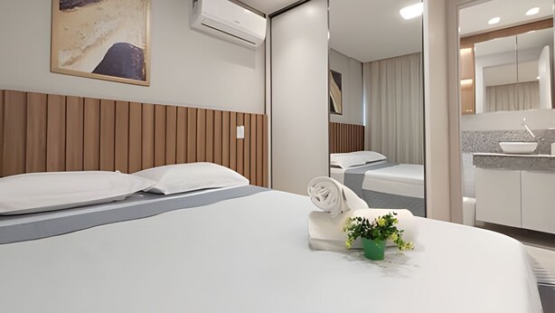 A hotel room with a bed, a green plant, and a painting on the wall. - Rio Park Ave -by TRH Home Stay (Jaboatão dos Guararapes)