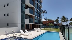 A modern building with a swimming pool, outdoor seating, and a clear sky. - Rio Park Ave -by TRH Home Stay (Jaboatão dos Guararapes)