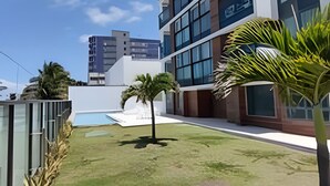 A modern building with a swimming pool, palm trees, and a clear sky. - Rio Park Ave -by TRH Home Stay (Jaboatão dos Guararapes)