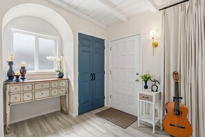 A hallway with a white console table, a blue door, a white door, a small white table with a lamp, and a guitar leaning against the wall. - Prime Central Location- Minutes from TMC Hospital: Desert House (Tucson)
