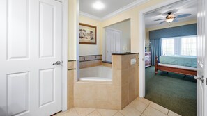A hotel room with a bathtub, a bed, a dresser, and a ceiling fan.