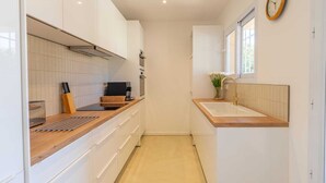 A narrow kitchen with white cabinets, a wooden countertop, a sink, and a clock on the wall.