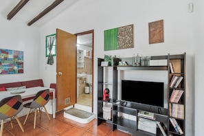 A living room with a fireplace, a bookshelf, a dining area with a table and chairs, and a door leading to another room. - Historic Juan Room with Mountain Views, Shared Terrace and Wi-Fi (Mogán)