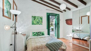 A bedroom with a bed, a bedside lamp, a green door, a mirror, and a view of the outdoors.