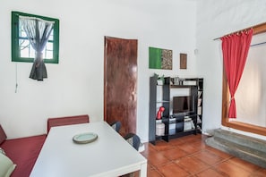Une pièce avec une table blanche, un canapé rouge, un meuble pour la télévision avec un téléviseur, et un rideau rouge.