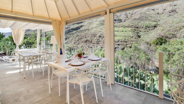 An outdoor dining area with white furniture and a view of a mountainous landscape.