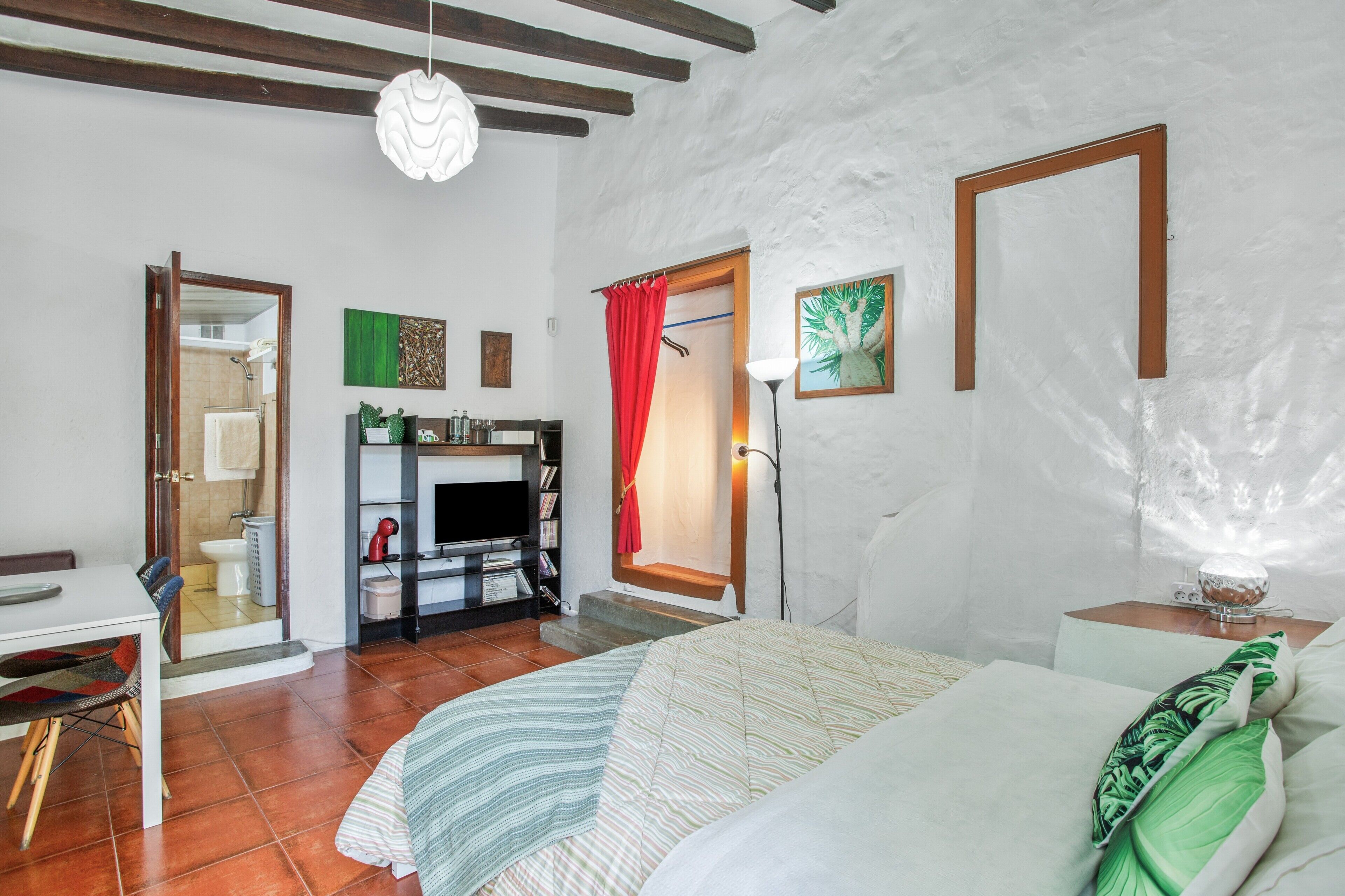 Un dormitorio con cama, escritorio, televisión y baño visible a través de una puerta abierta.