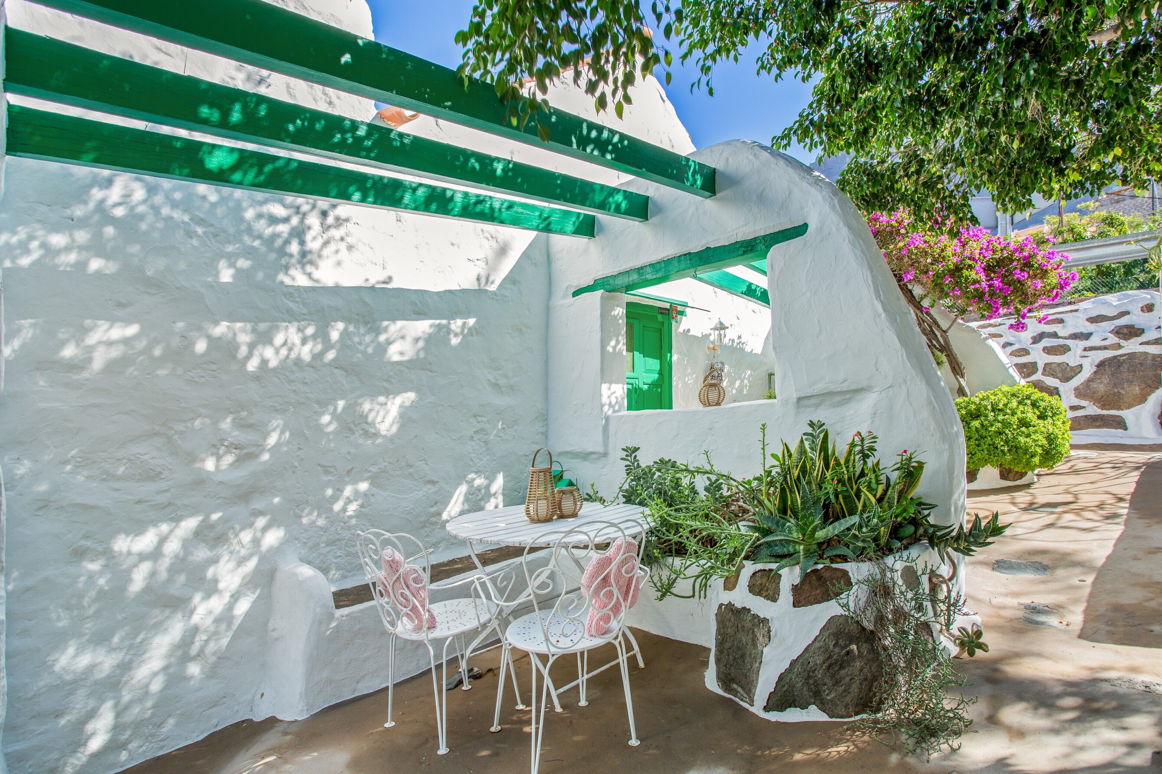 A white building with green accents, a small table with chairs, and potted plants.