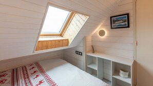 A bedroom with a skylight, a bed, a shelf with a picture, and a wall-mounted light.