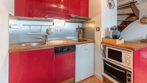 A compact kitchen with red cabinets, a dishwasher, a microwave, and a coffee machine.